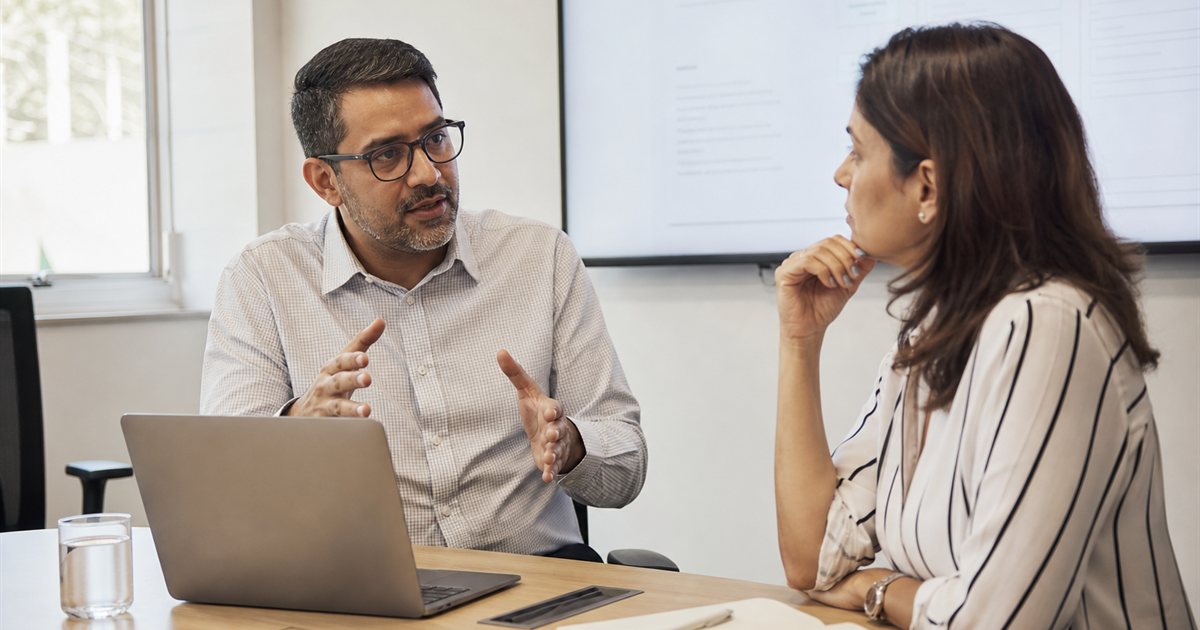 Duas pessoas conversando sobre um projeto ao lado de um notebook